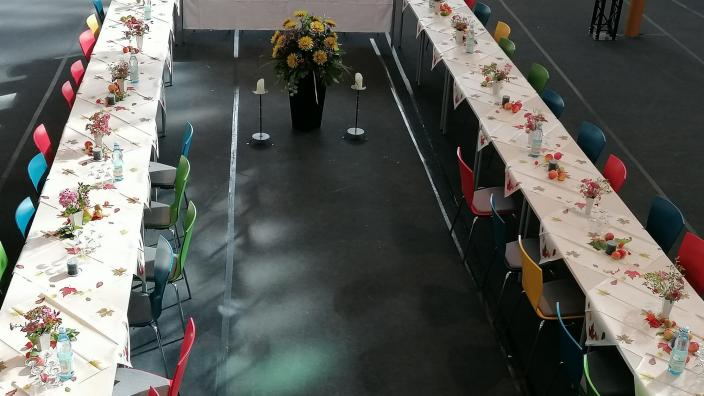 gedeckte und blumengeschmückte Tische als u-förmige Tafel aufgestellt, mit bunten Stühlen, in der Mitte eine große Blumenstaude und rechts und links je ein Kerzenständer